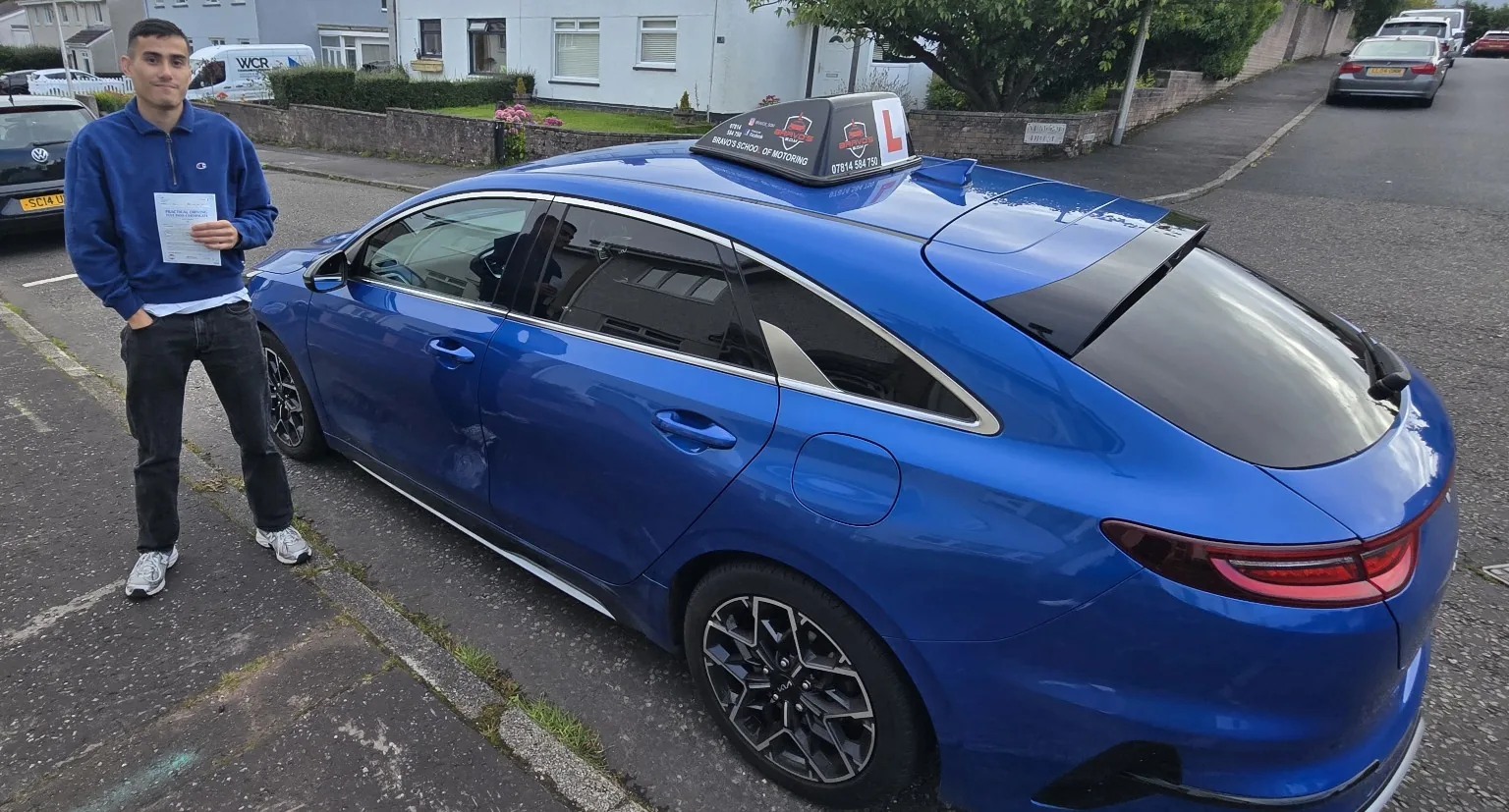 Successful Bravo's pupil with pass certificate beside blue learner car